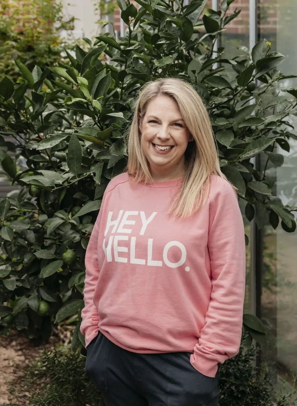 Dietitian and Supervisor Louise Grech standing in front of a hedge and wearing a pink jumper that says "Hey Hello"