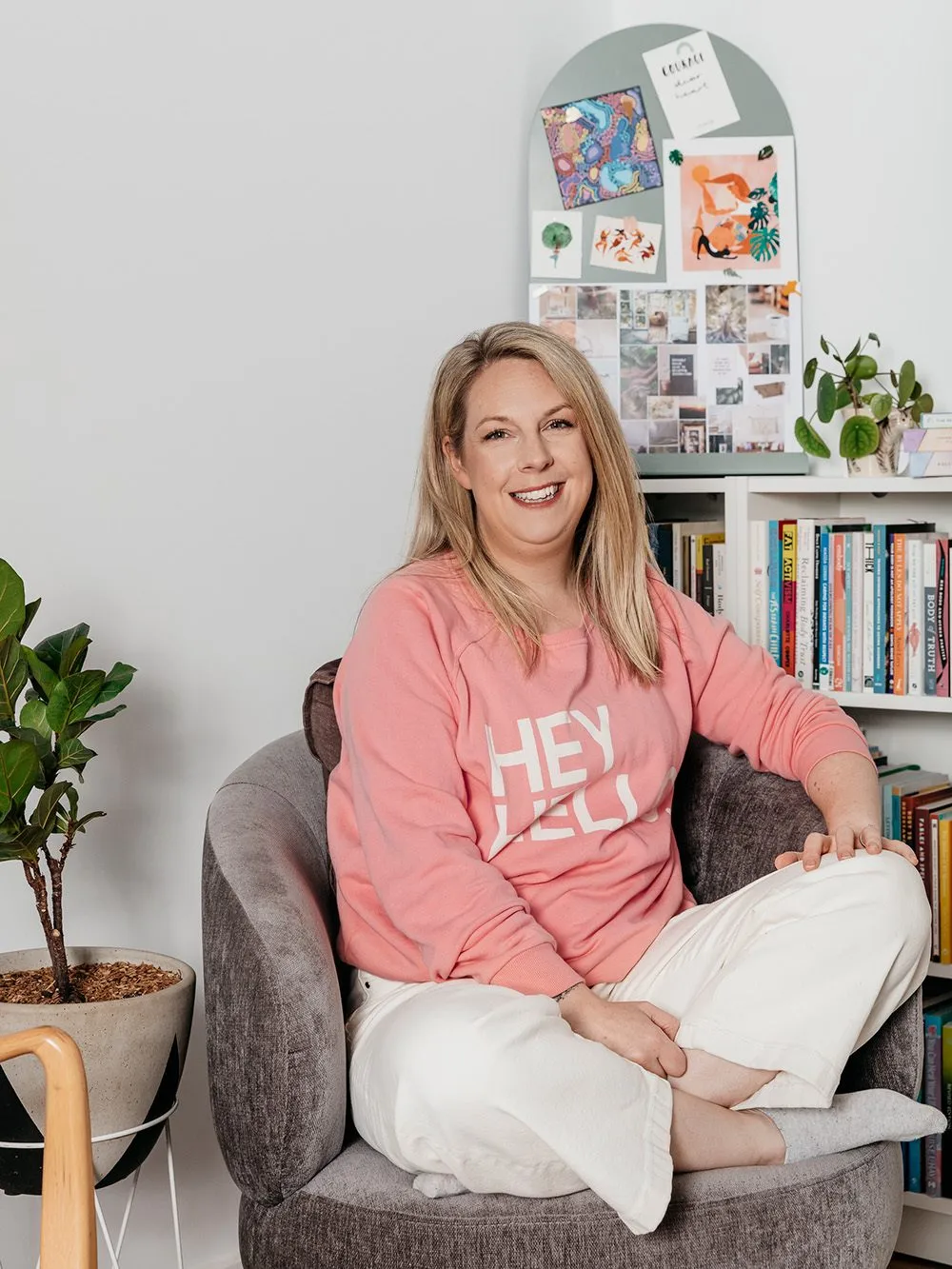 Dietitian and Supervisor Louise Grech sitting in a grey armchair and wearing a pink jumper that says "Hey Hello". Behind her is a bookshelf and mood board.